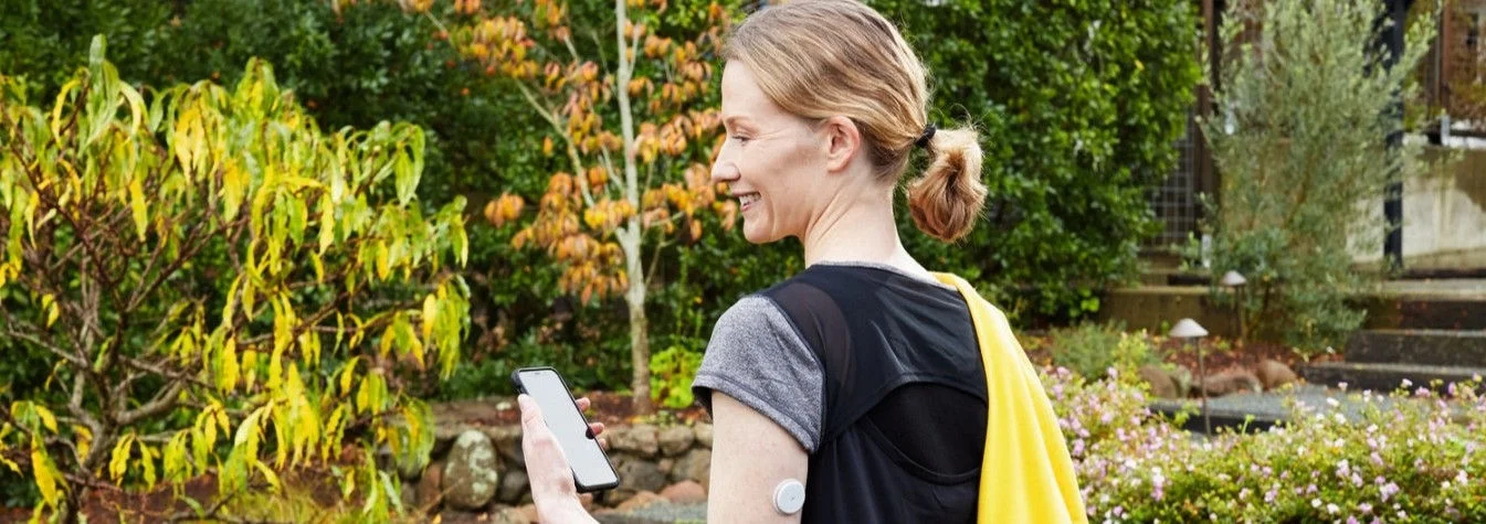 Pessoa caminhando em área externa com smartphone na mão e sensor FreeStyle Libre 2 Plus visível no braço