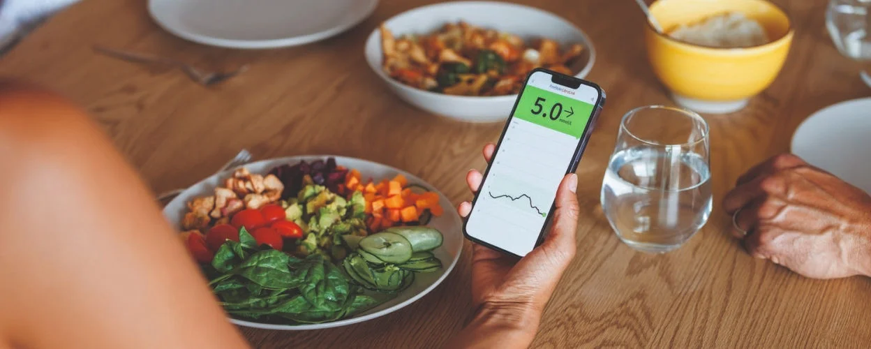 A man wearing a FreeStyle Libre sensor chooses healthy vegetables from a buffet at an outdoor social gathering.