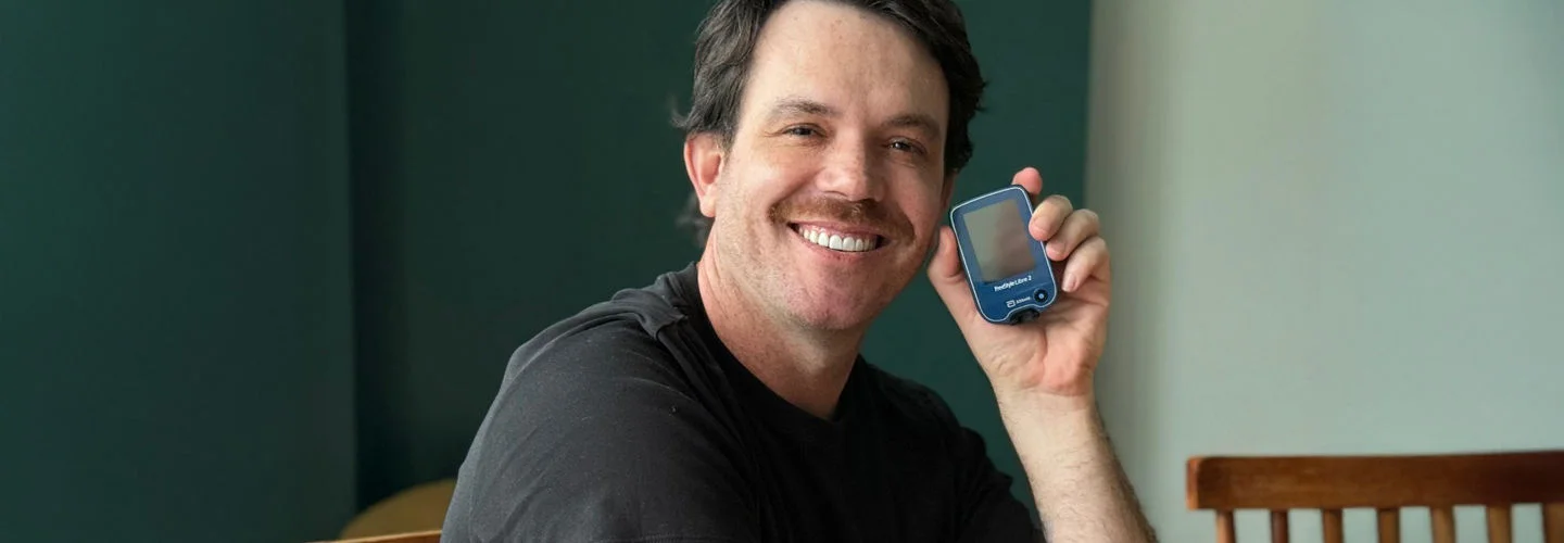 Pessoa sentada à mesa segurando um glicosímetro na mão direita