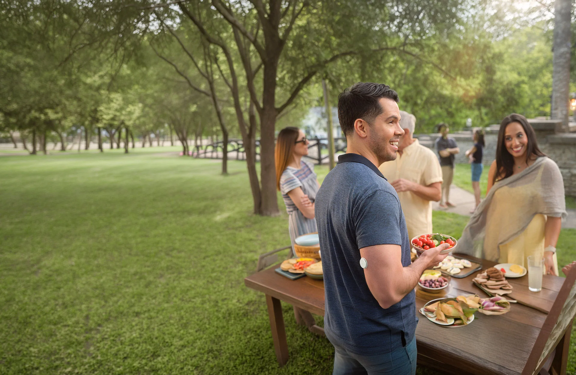 A man in a blue t-shirt with a FreeStyle Libre sensor on his left arm joyfully swinging his kid in the air.