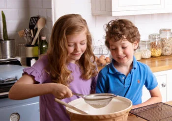 Duas crianças em uma cozinha, peneirando farinha