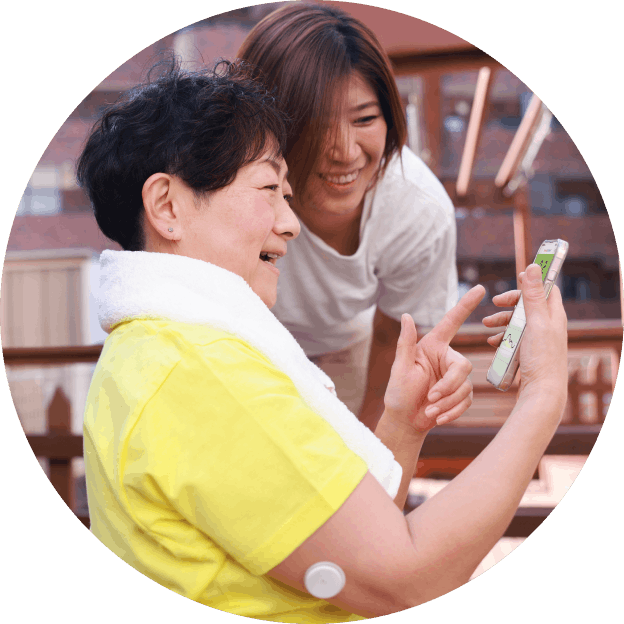 Older woman wearing a FreeStyle Libre sensor on her upper arm smiles while a younger woman leans in to look at glucose data on a smartphone.