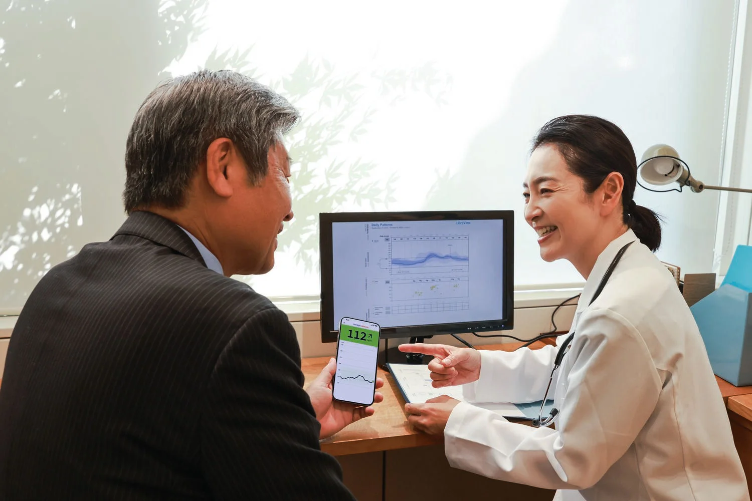 Asian Healthcare provider caring for Asian diabetic patients in modern healthcare environments. 
Healthcare provider installing the sensor, discussing medical records and showing the patient how to correctly check their glucose levels on their reader or mobile phone.