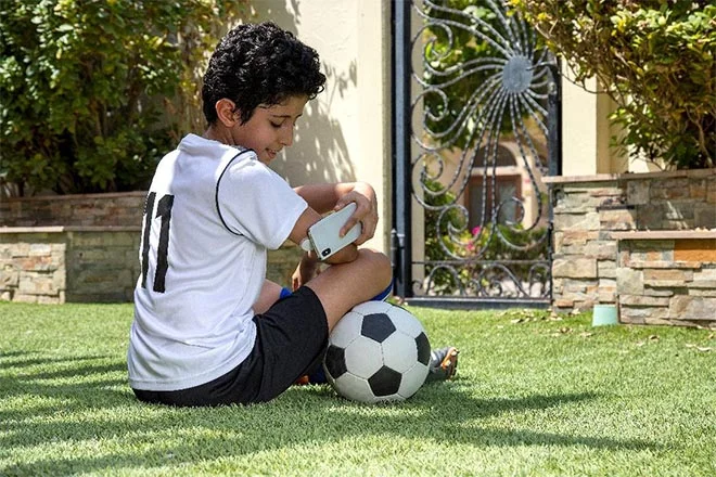 Garoto sentado na grama com uma bola de futebol, enquanto faz um scan com seu smartphone do sensor FreeStyle Libre