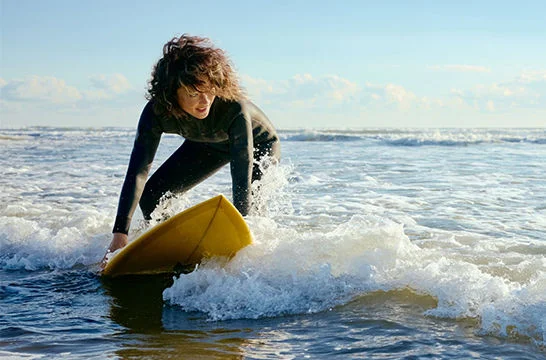 Person in shallow ocean water practicing on a surfboard as small waves break around the board.