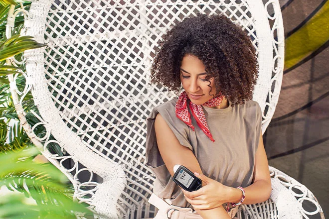 Mulher vestindo uma camisa marrom utilizando um sensor FreeStyle Libre no braço, e medindo seus niveis de glicose por meio de um scan com o leitor FreeStyle Libre