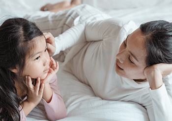 Mother laying next to her daughter on a bed