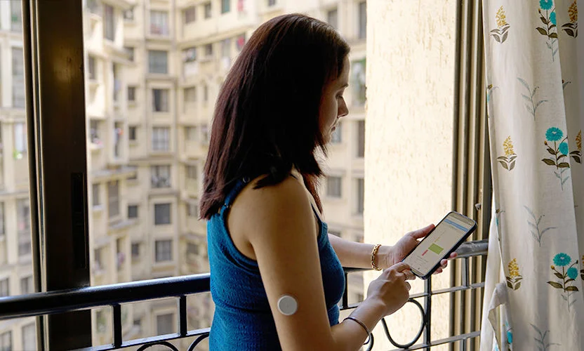 A woman wearing a sensor showing her glucose data on her phone with her husband.