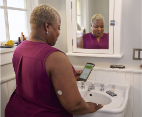 Mulher em frente ao espelho verificando seus dados de glicose no celular