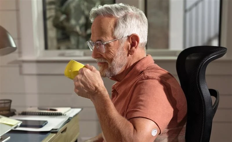 Person påfører sensor på overarm i et lyst rum