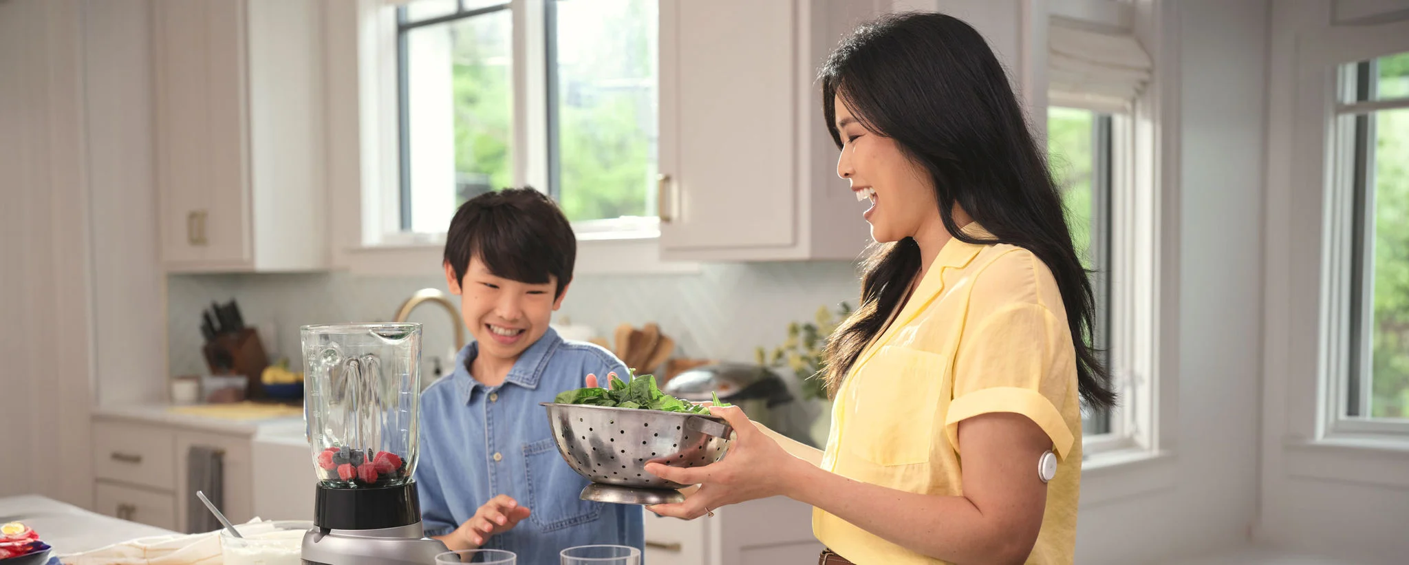 A mother cooks with her son in a bright kitchen, with a FreeStyle Libre sensor on her upper arm.