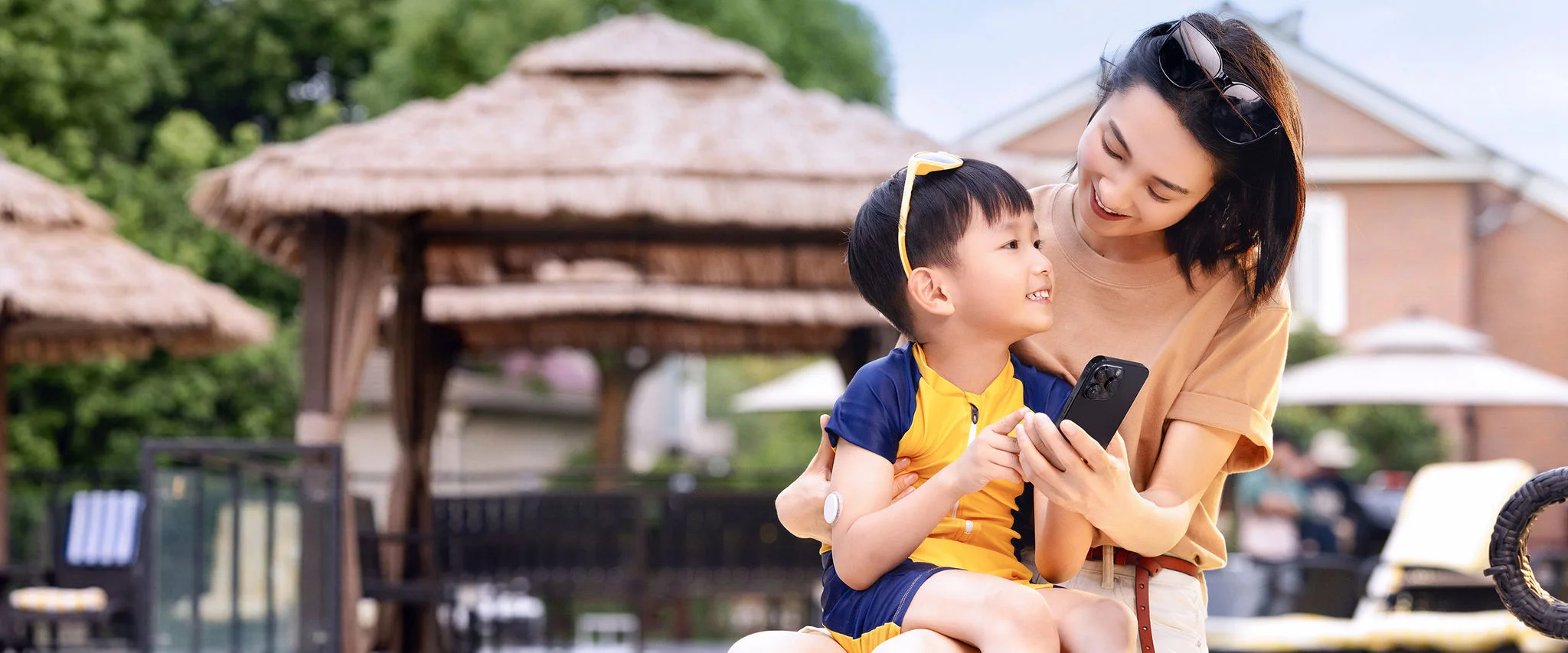 A smiling mother and her son, his glucose sensor visible, lean together over a smartphone to check his glucose level.