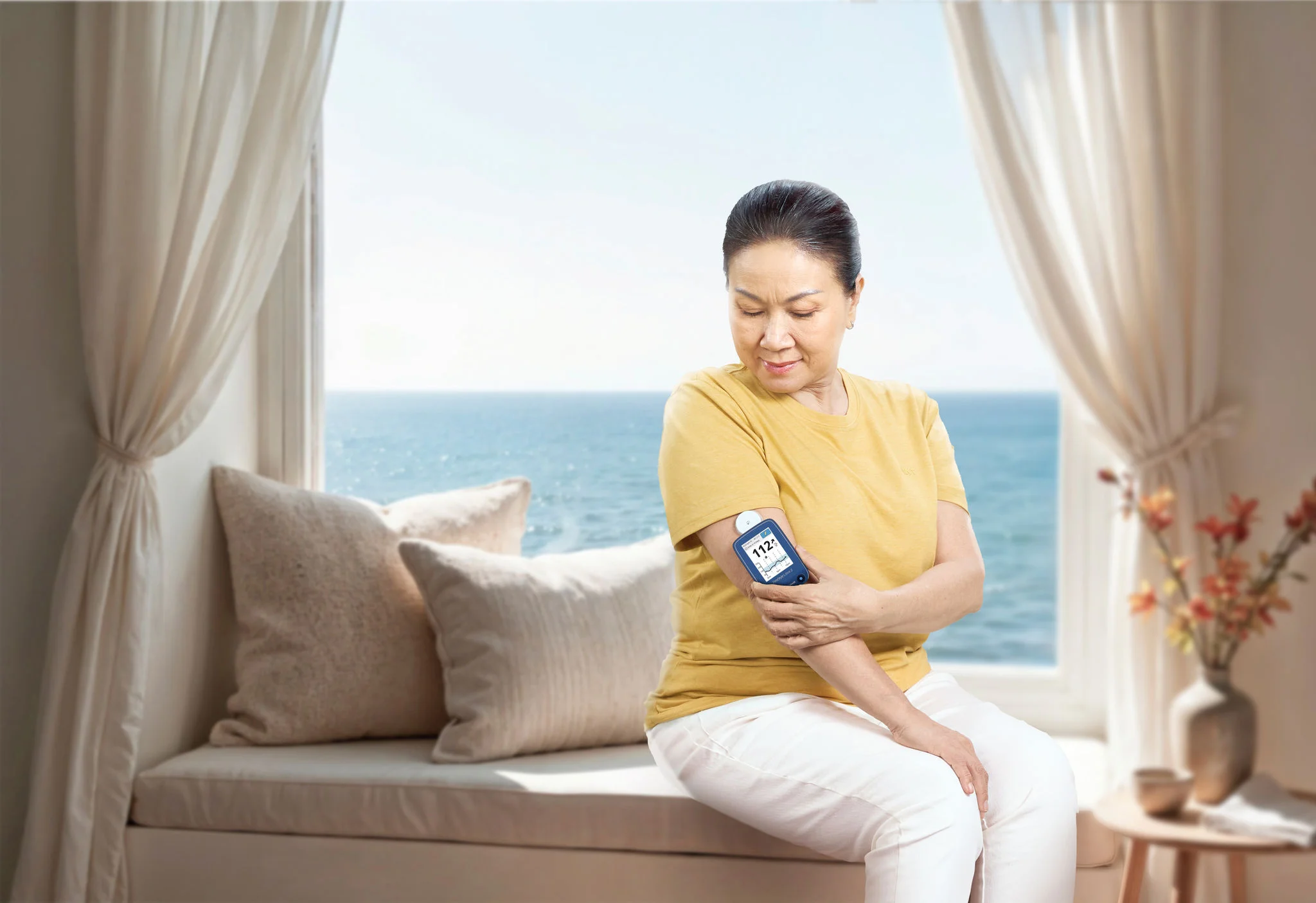 Một người trong bếp đang chạm vào thiết bị cảm biến trên cánh tay và cầm máy đọc chỉ số, với quầy bếp sáng và gọn gàng phía sau.