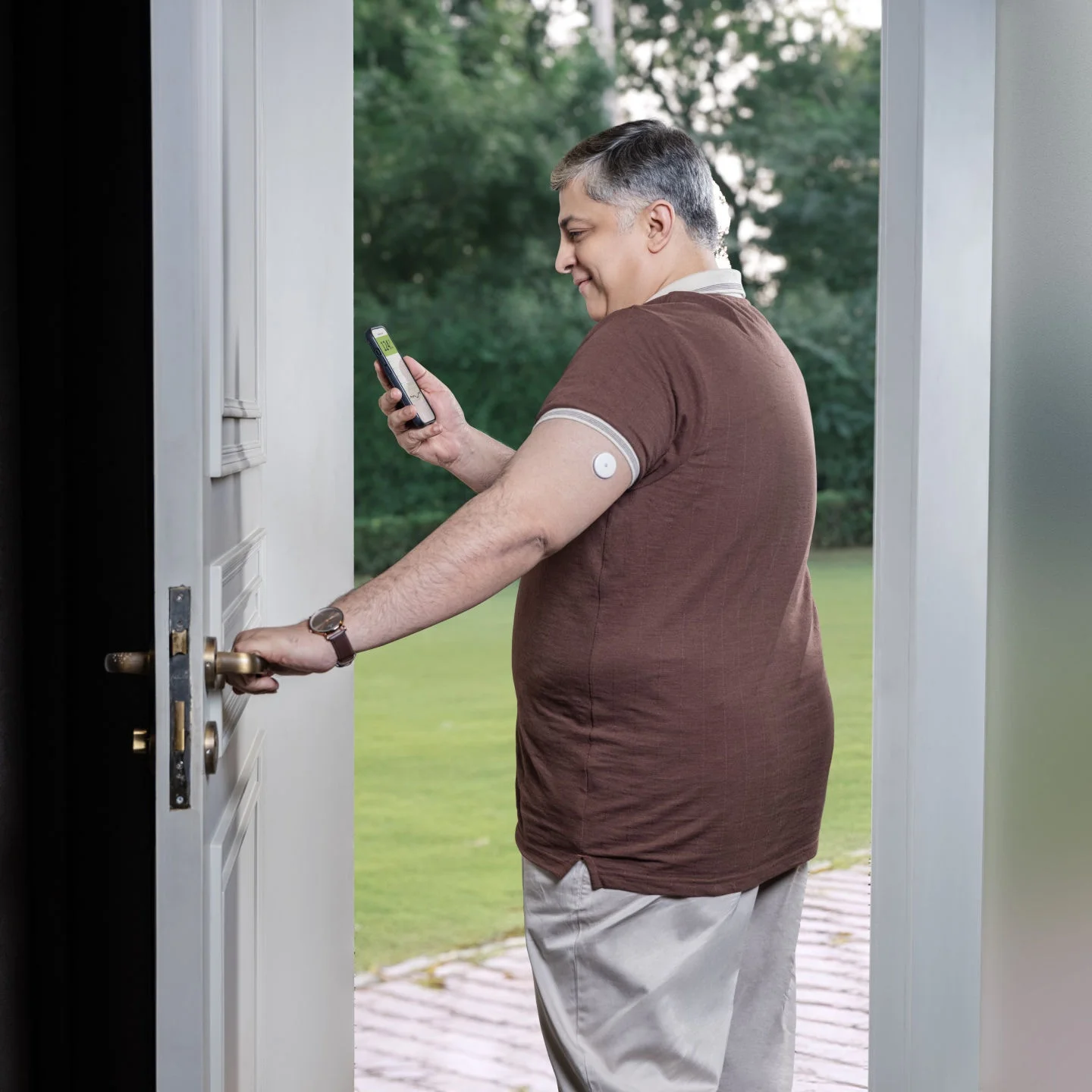 A man checking his smartphone in a doorway with a glucose sensor on his arm.