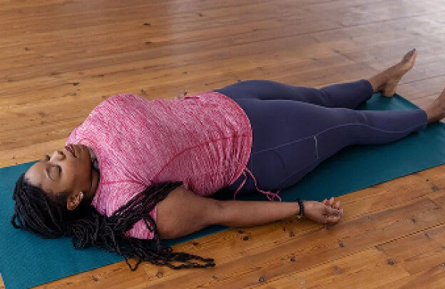 Mujer recostada sobre una colchoneta, relajando el cuerpo y la mente durante un ejercicio de respiración consciente.