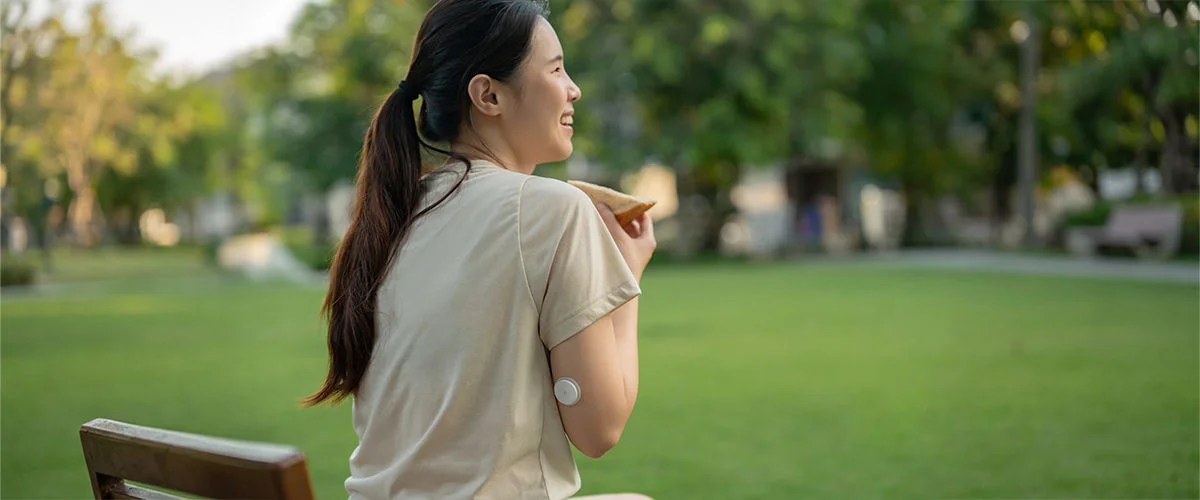 Women wearing a FreeStyle Libre sensor on the upper arm while standing outdoors in a park setting.