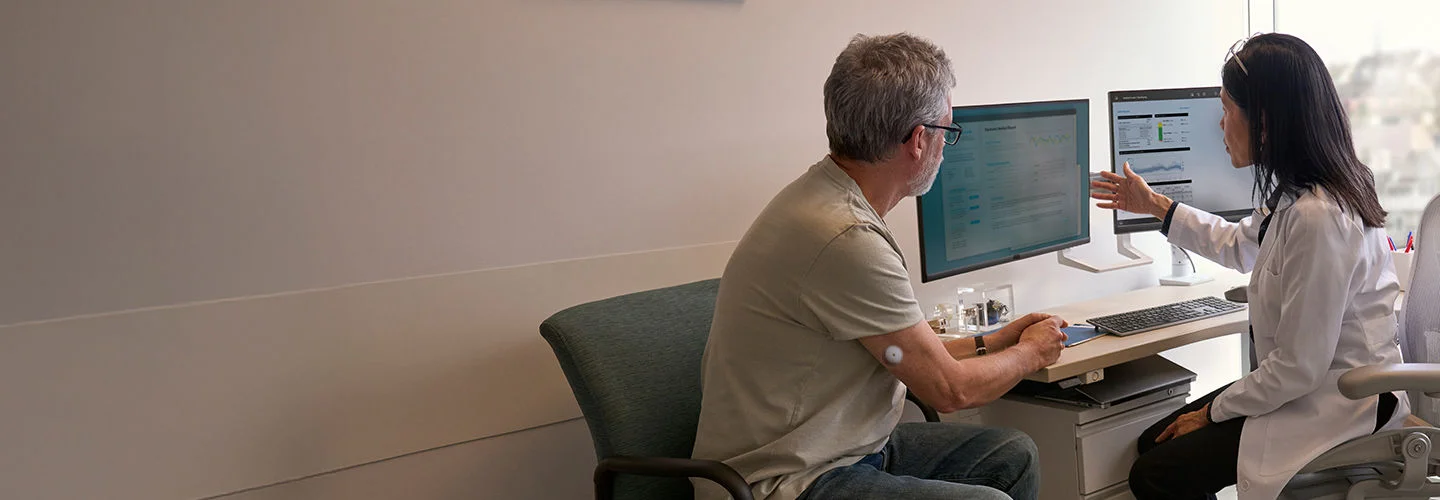 一名男性患者坐在診間內，與身穿白袍的醫師討論，兩人面對電腦螢幕，醫師手指向螢幕解釋 LibreView 上的數據。