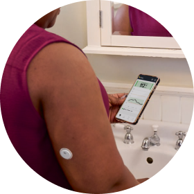 Woman in the bathroom staring at her phone while wearing a FreeStyle Libre 3 Plus sensor