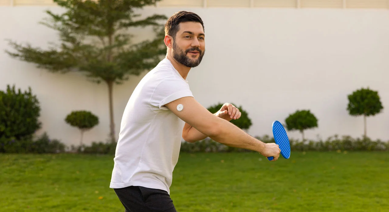 A man outdoors wearing a FreeStyle Libre sensor while playing raquet.