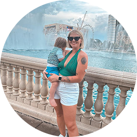 A woman wearing a sensor and holding her child in front of a fountain.