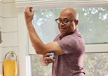A man applying his FreeStyle Libre sensor on  the upper back of his left arm.