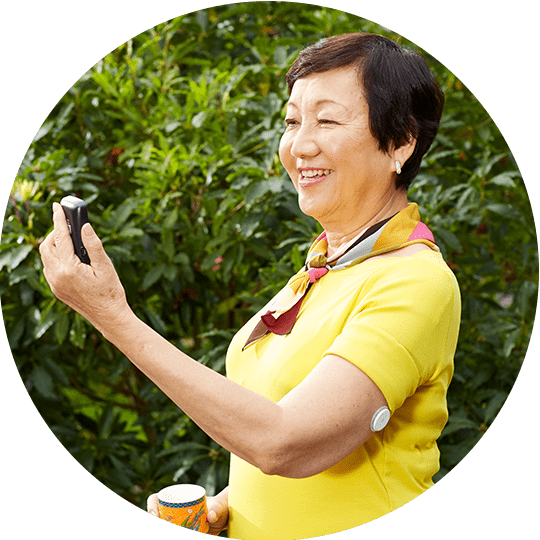 A smilling woman wearing a FreeStyle Libre sensor looking at her FreeStyle Libre reader