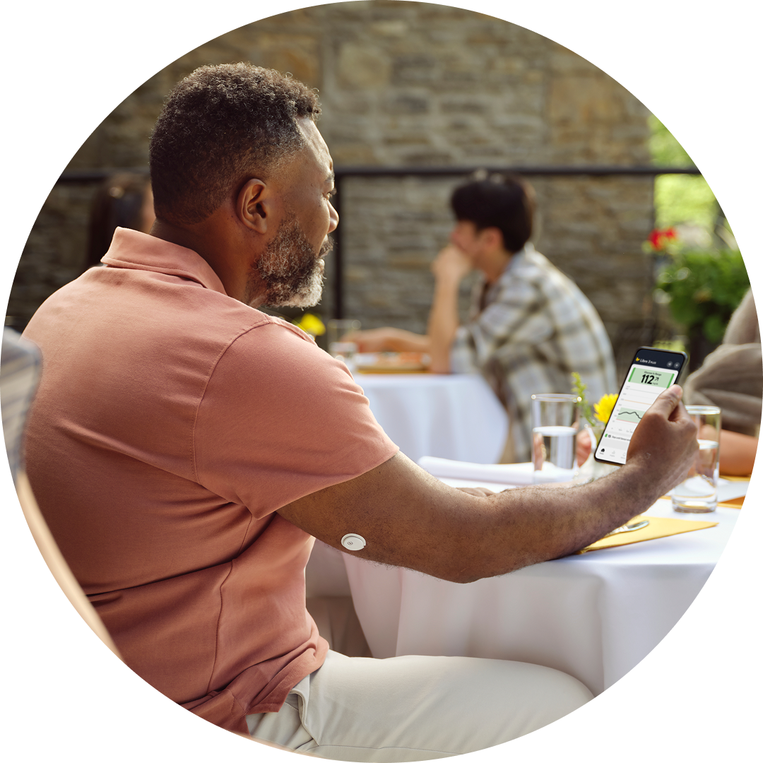 .Person seated outdoors holding a smartphone with a glucose reading, illustrating FreeStyle Libre apps and data sharing.