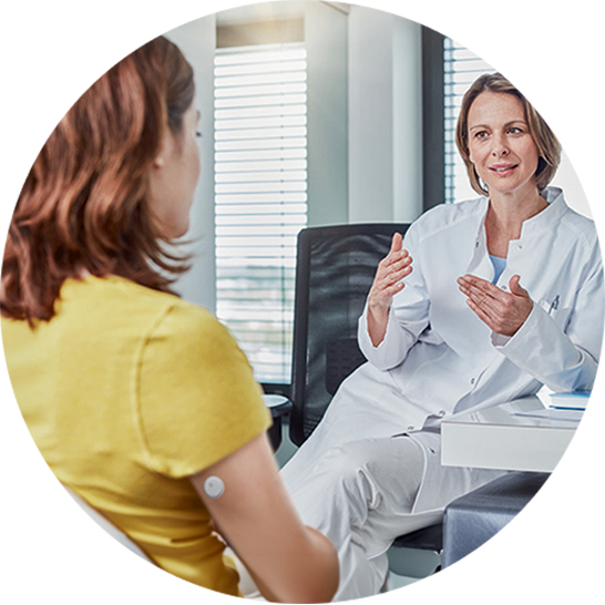 Person wearing a CGM sensor on the upper arm consulting with a healthcare professional in a medical office.
