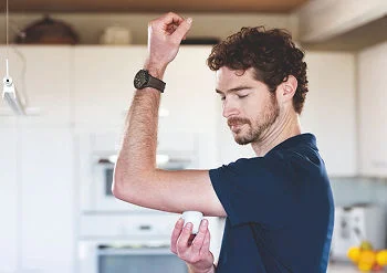 Person raising an arm while applying a FreeStyle Libre glucose sensor in a kitchen, with text about getting started using the system.