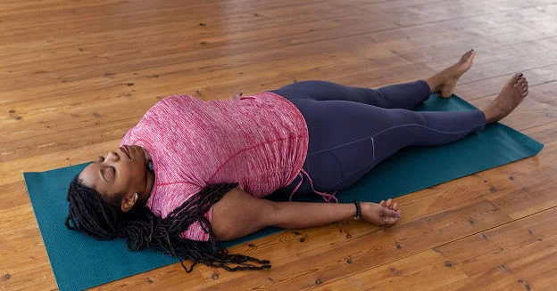 A woman lies on her back on a mat in a yoga pose, a popular way to boost holistic health.