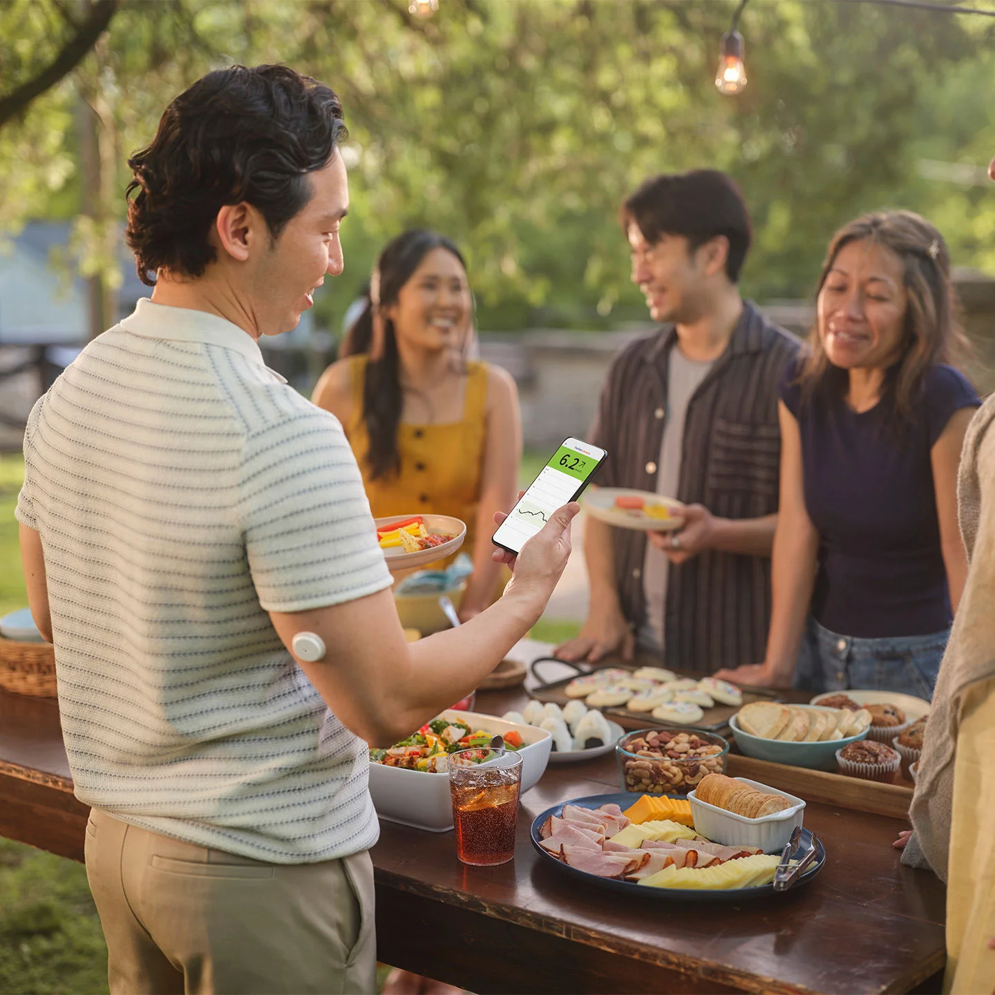 A man at an outdoor gathering  with a FreeStyle Libre sensor on his upper arm checks his glucose levels on his smartphone.