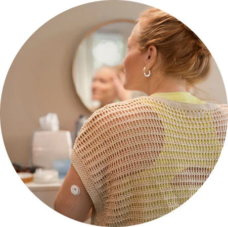 Woman standing by the mirror while wearing a FreeStyle Libre 3 Plus sensor