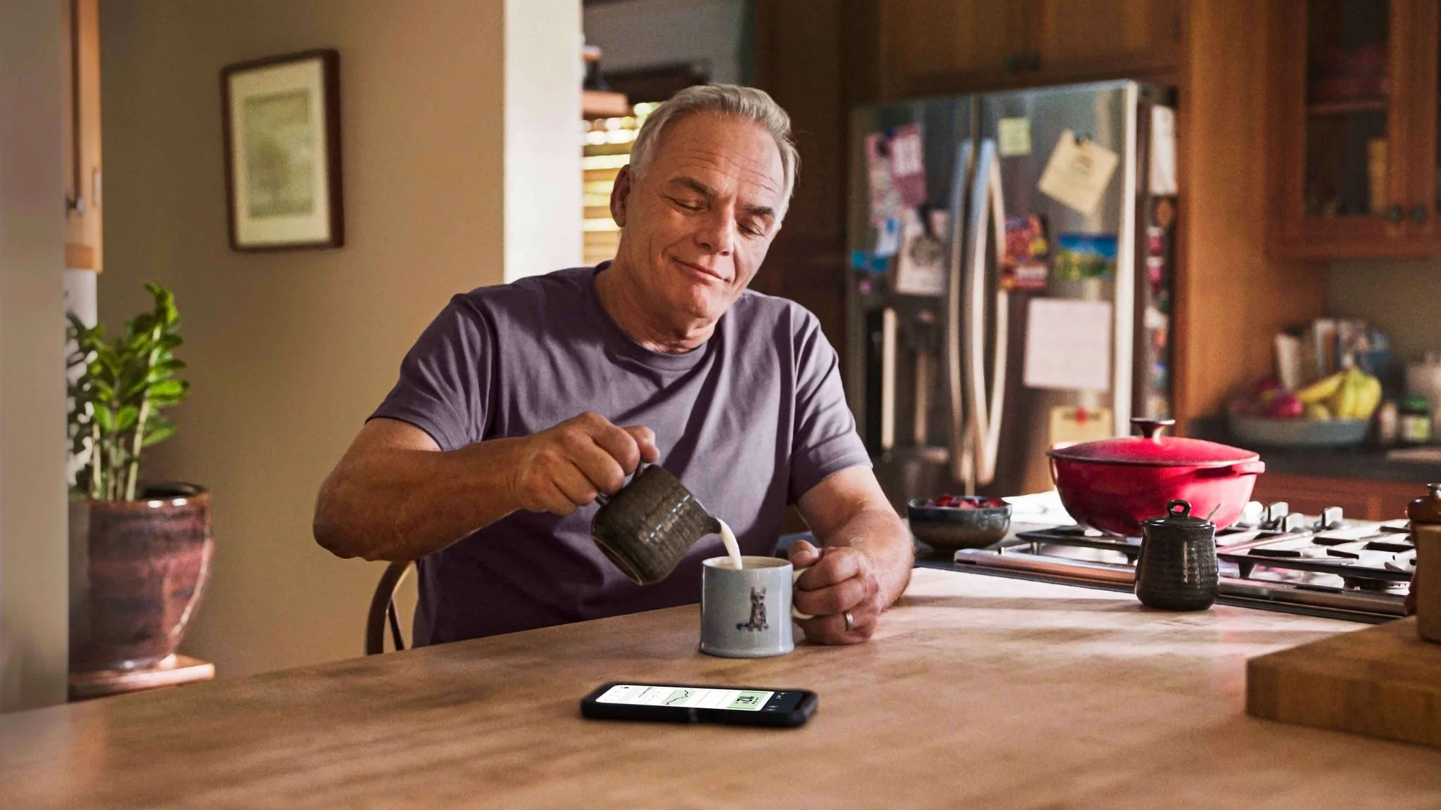 Hombre tomando una taza de café en la cocina, sonriendo mientras disfruta un momento de calma.