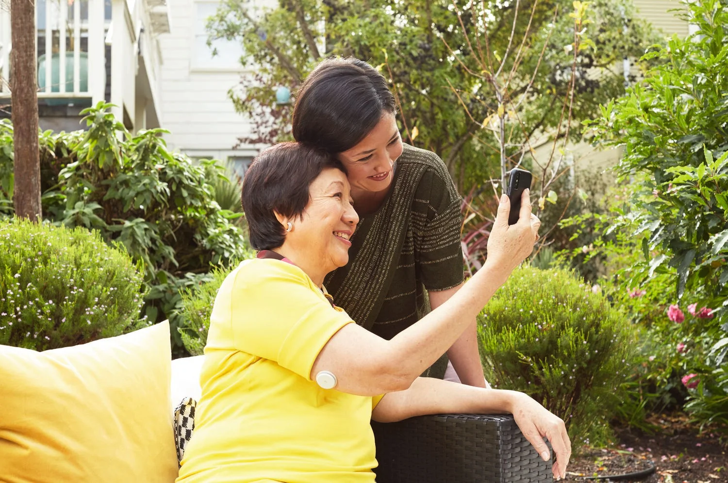 A woman wearing a FreeStyle Libre sensor hugs laughs with her daughter in her lap.