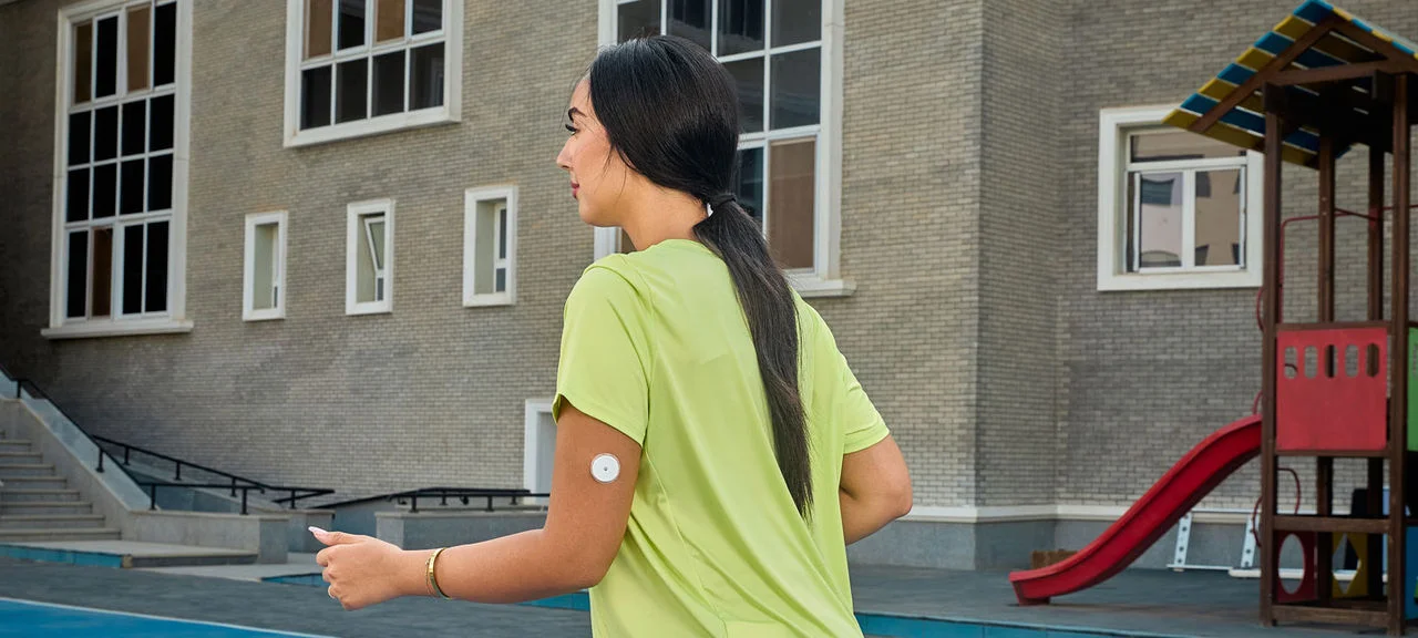 A woman wearing a Freestyle Libre sensor balancing on an exercise ball while smiling broadly.