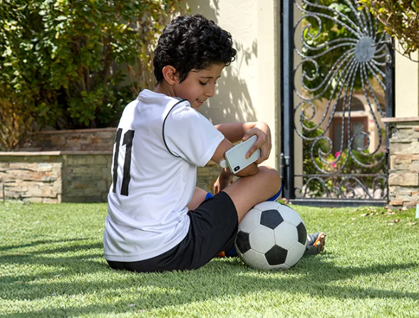 Garoto sentado na grama com uma bola de futebol, enquanto faz um scan com seu smartphone do sensor FreeStyle Libre