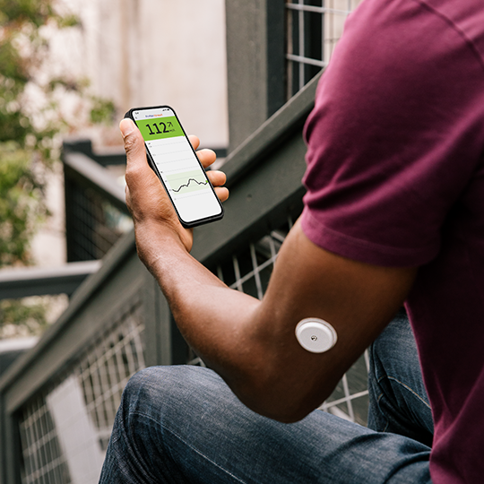 一名男士左手臂配戴 FreeStyle Libre2 傳感器，手持智慧型手機，正看著 LibreLink 應用程式上的葡萄糖數值。