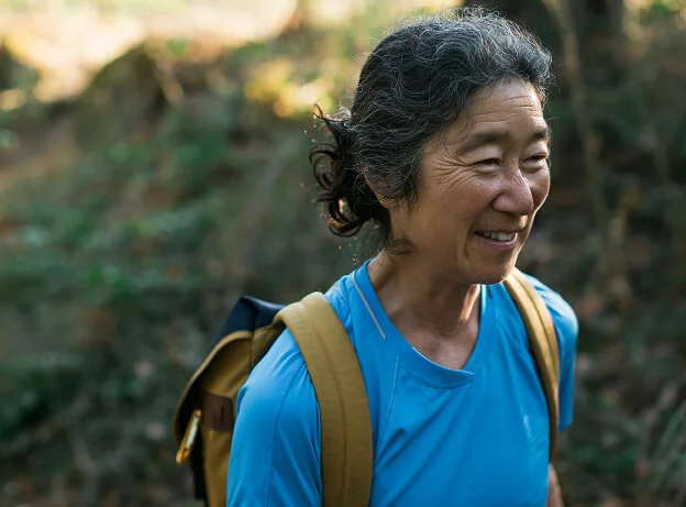 Mujer caminando entre árboles, sonriente y relajada, disfrutando de la naturaleza