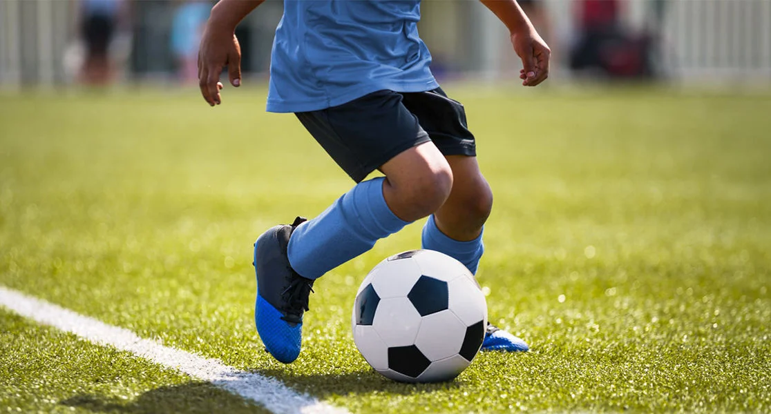 Close-up of a youth soccer player dribbling a soccer ball on a grass field during a game or practice.