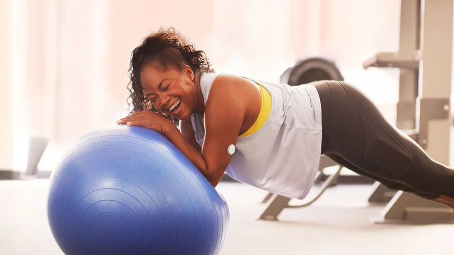 Woman with a FreeStyle Libre sensor on her arm smiling while balancing on a gym ball