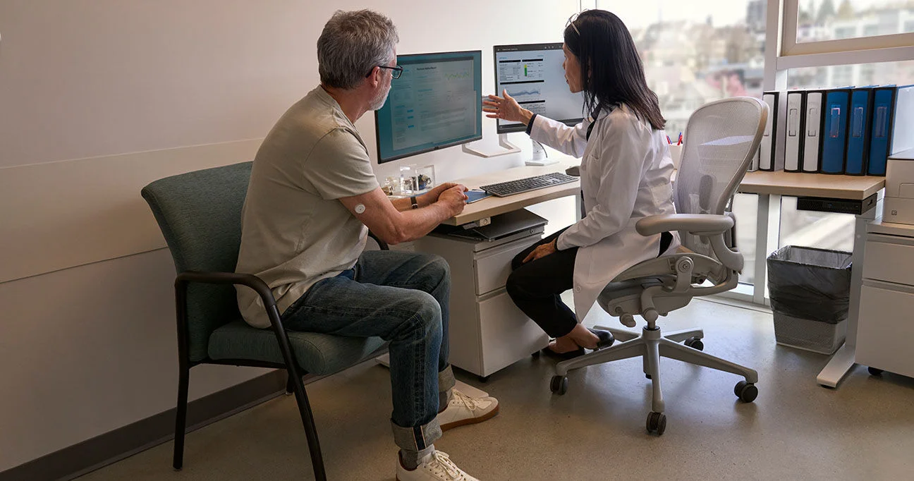 Médica e paciente analisam relatórios do LibreView durante consulta; o paciente usa o sensor FreeStyle Libre 2 Plus no braço.