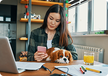 Mujer trabajando en casa con su perro revisa su celular