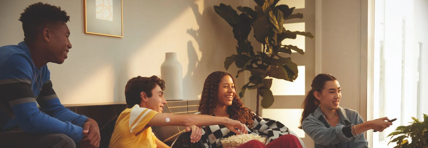 Quatro pessoas reunidas em uma sala de estar com decoração moderna e com plantas. Todas voltadas para o lado direito da imagem, como se estivessem assistindo ou comentando algo.