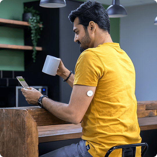 A man wearing a FreeStyle Libre sensor looking at his app next to an inset image of the smartphone app screen.