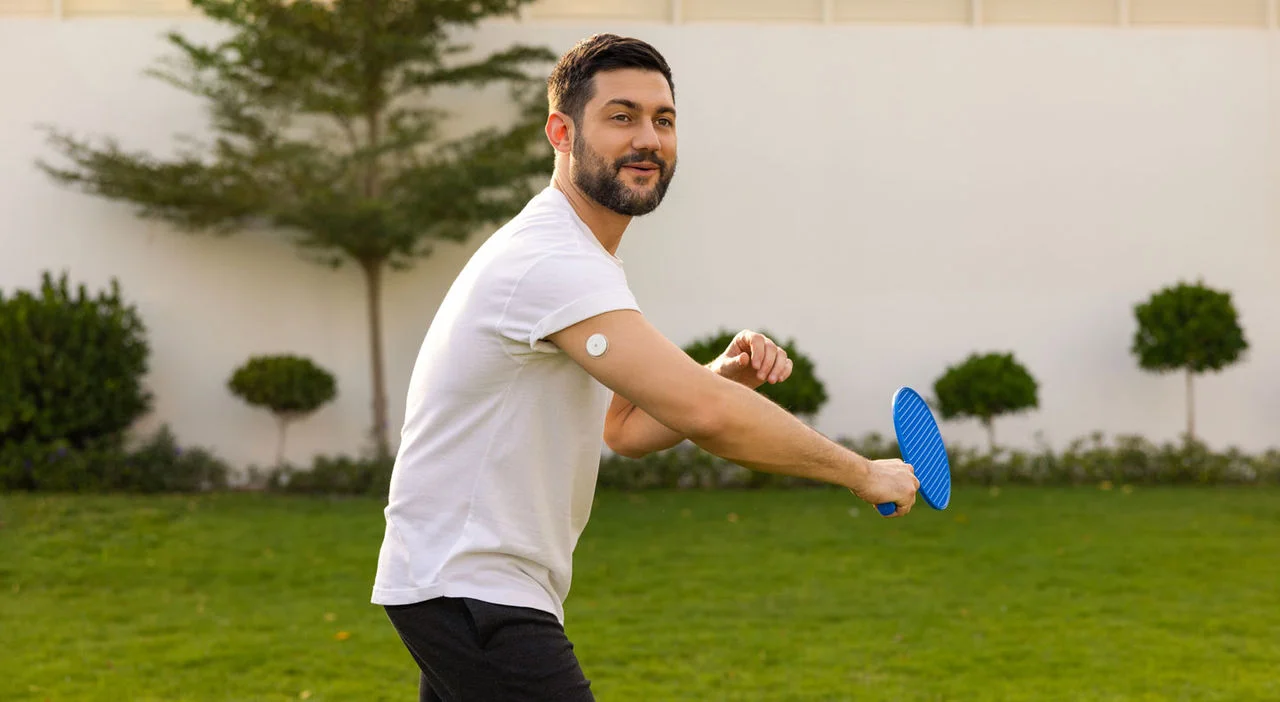 A man outdoors wearing a FreeStyle Libre sensor while playing raquet.