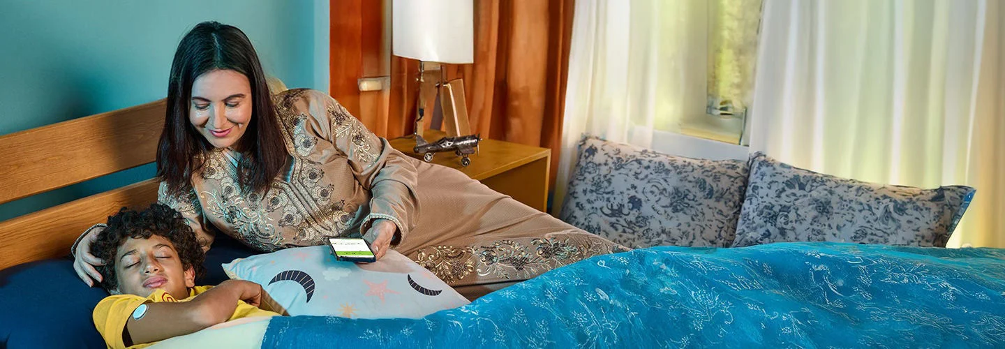 A woman sitting next to her son in the bed. The boy is wearing a freestyle libre sensor.