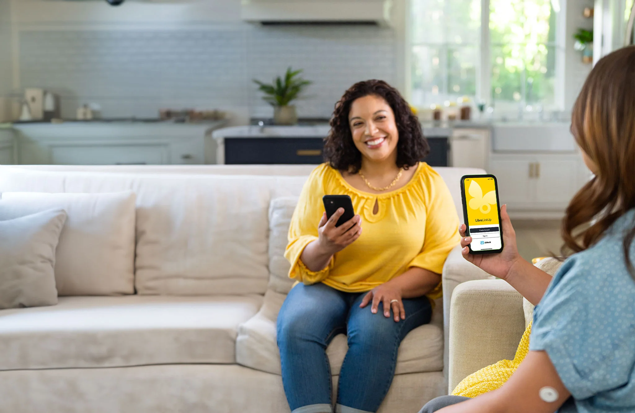 Person at home holding a smartphone while another phone displays the LibreLinkUp app, illustrating sharing glucose data with caregivers.