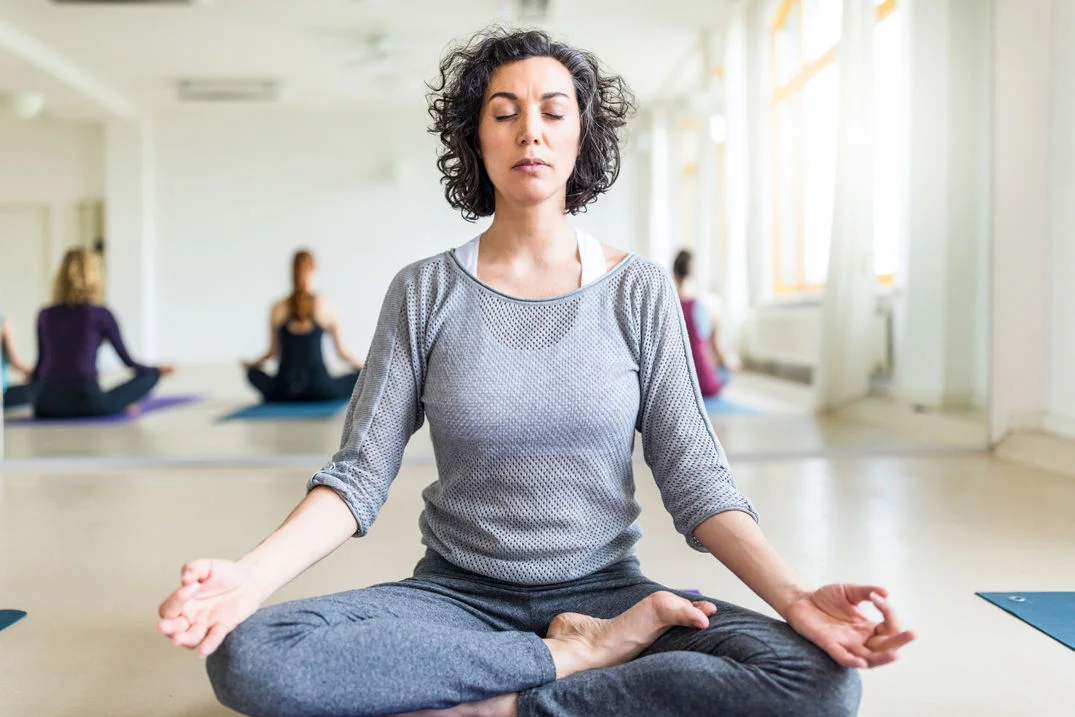 Mujer meditando en un ambiente tranquilo, con los ojos cerrados y una expresión relajada, practicando mindfulness.