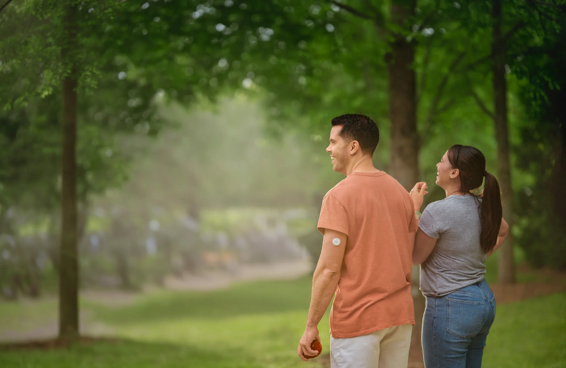 Dos personas paradas en un parque, una con un sensor de glucosa en el brazo.