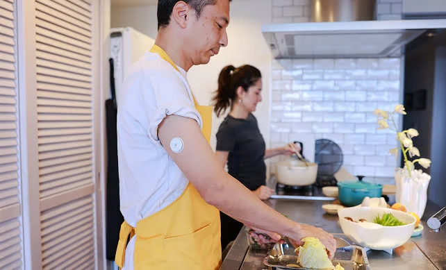 A man wearing a FreeStyle Libre sensor prepares fresh ingredients for a meal while cooking together with his wife.